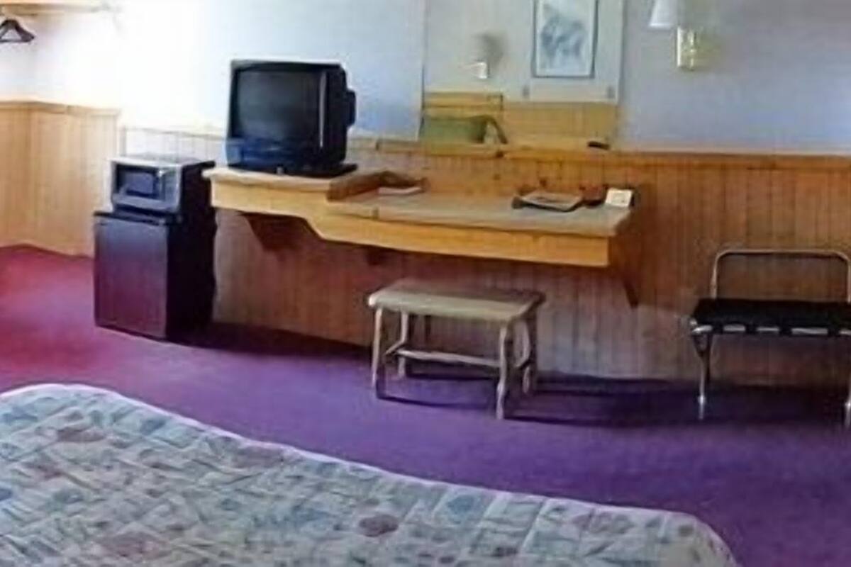 Una habitación pequeña y funcional con dos camas individuales, un escritorio con silla, televisor y una mesita.