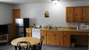 Una cocina compacta con armarios de madera, refrigerador, estufa, microondas, lavamanos y una mesa de comedor con sillas.