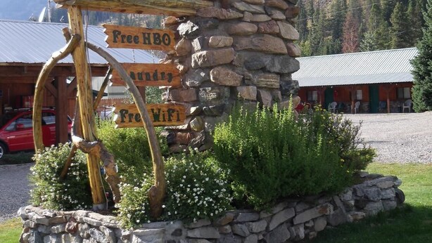 Señal del Hotel Alpine, con una rústica pared de piedra y un poste de madera.