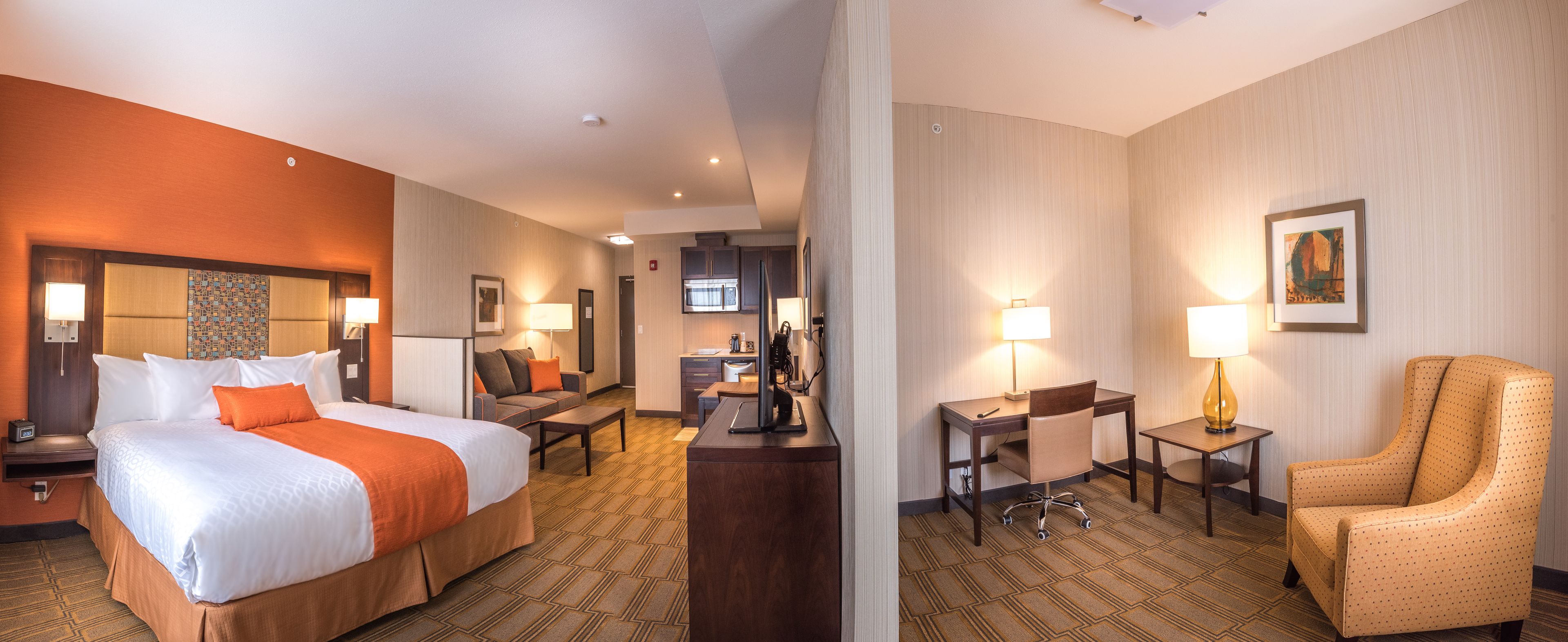 A hotel room with a large bed, a desk, a chair, and a sofa.