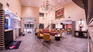 A hotel lobby with a reception desk, a large chandelier, a seating area with sofas and chairs, and a large wall painting. - Best Western Plus Chateau Fort St. John (Fort St. John)