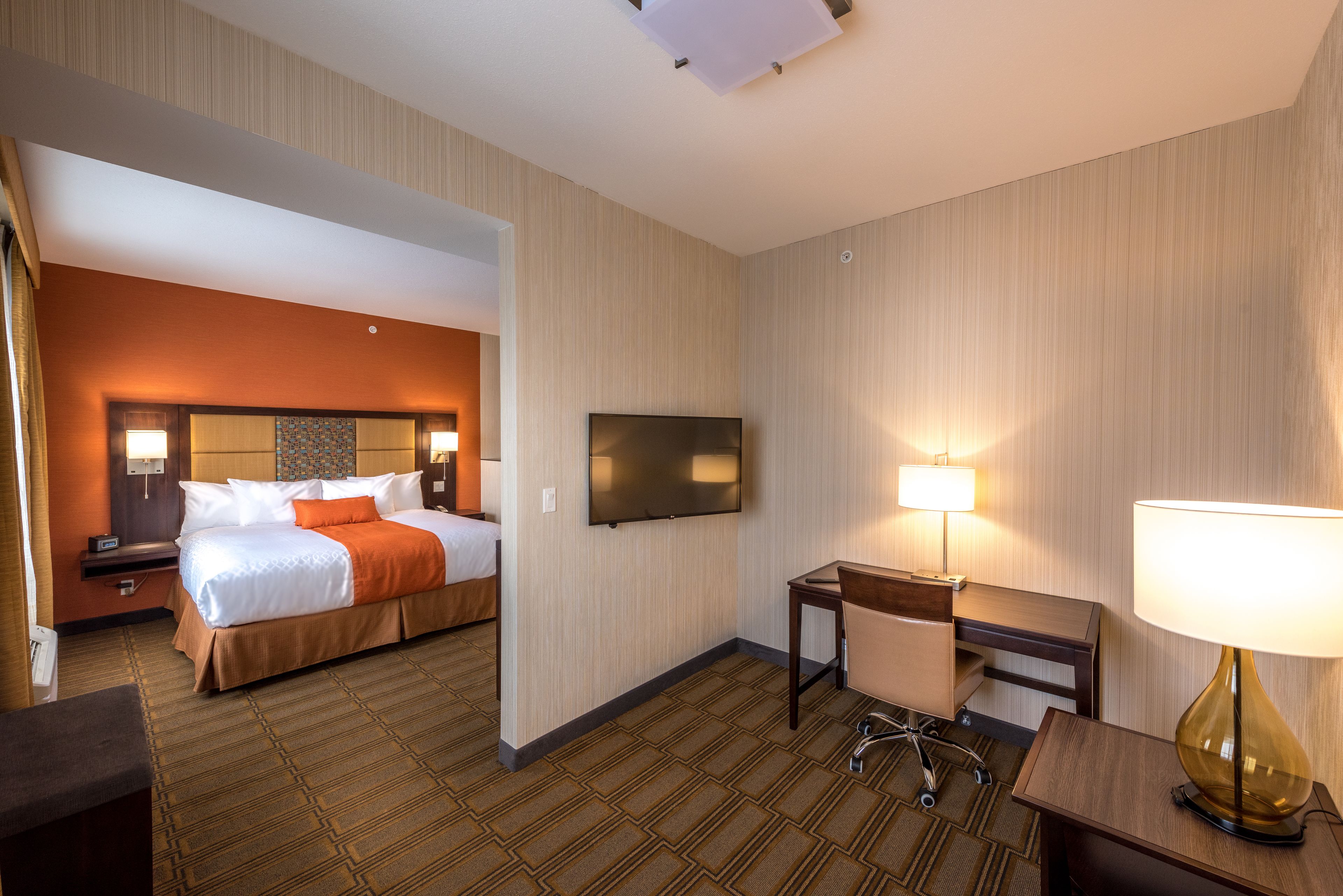 A hotel room with a bed, a desk, a chair, a TV, and a lamp.