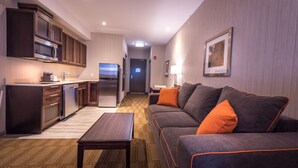 A modern hotel room with a kitchenette, a sofa with orange cushions, a flat-screen TV, and a framed picture on the wall. - Best Western Plus Chateau Fort St. John (Fort St. John)
