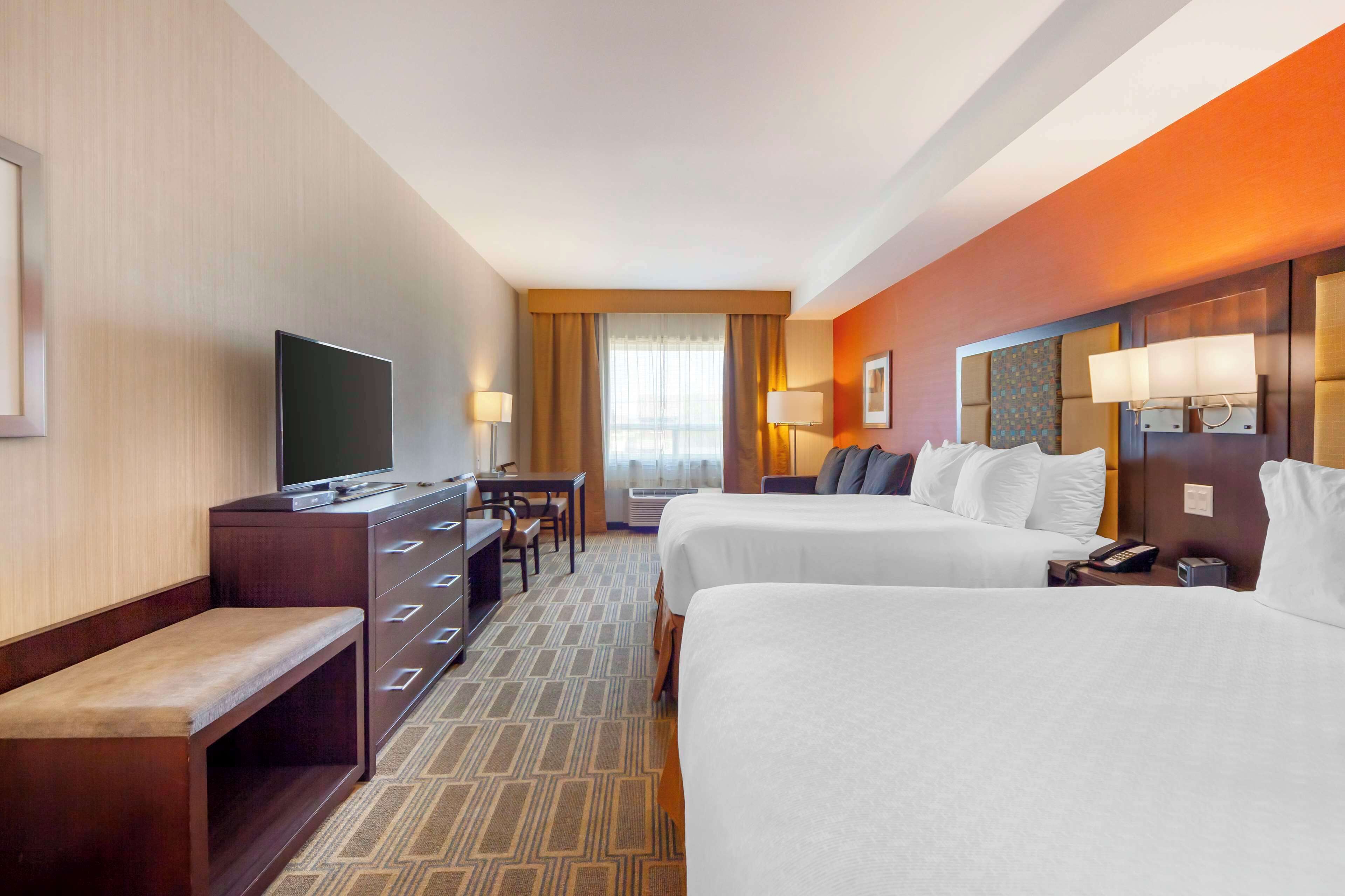 A hotel room with two beds, a desk with a TV, a dresser, and a bench.