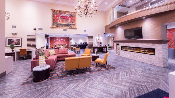 A spacious lobby with a modern fireplace, comfortable seating, a large artwork on the wall, and a high ceiling with a chandelier. - Best Western Plus Chateau Fort St. John (Fort St. John)