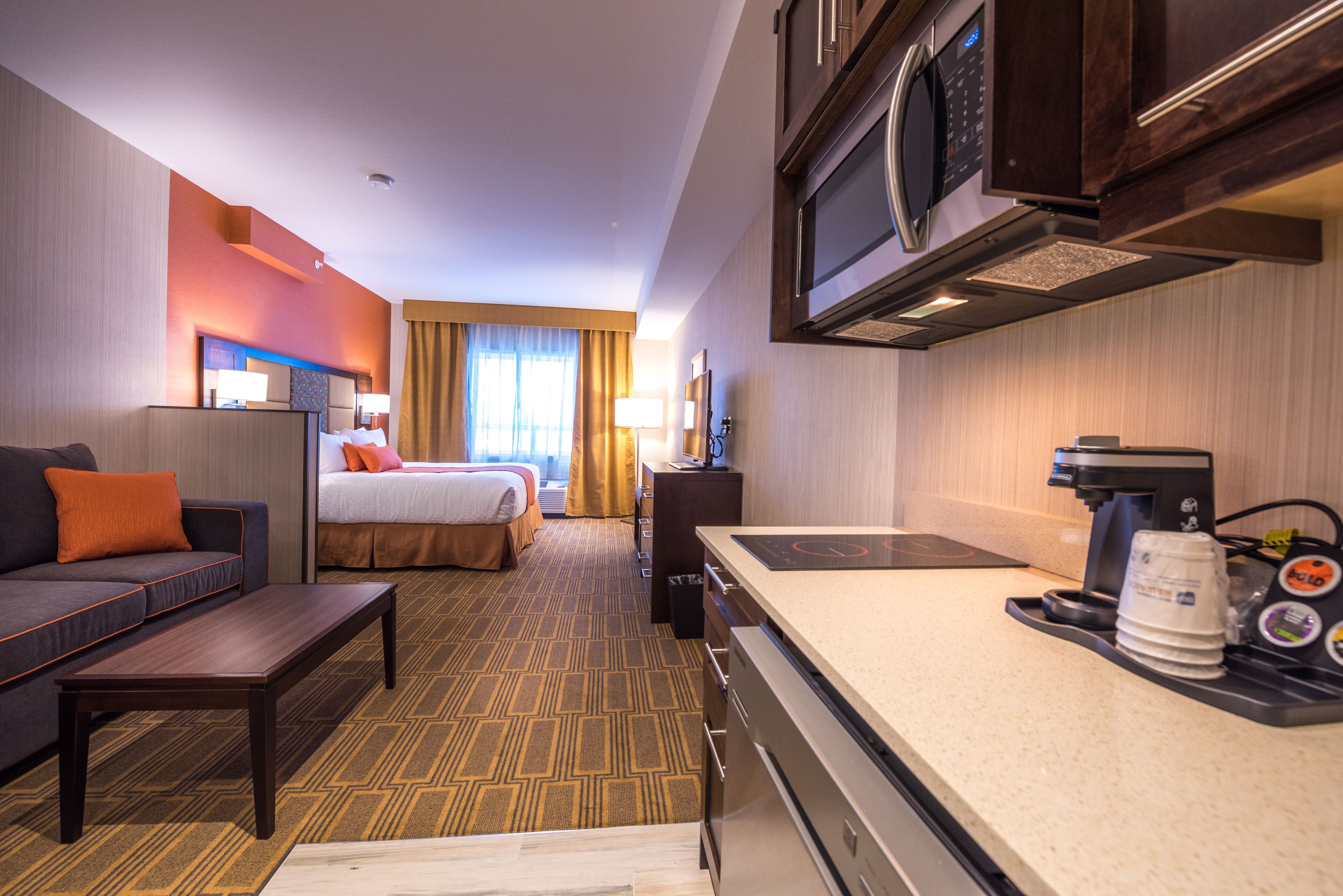 A hotel room with a bed, a sofa, a desk, a microwave, and a coffee maker.
