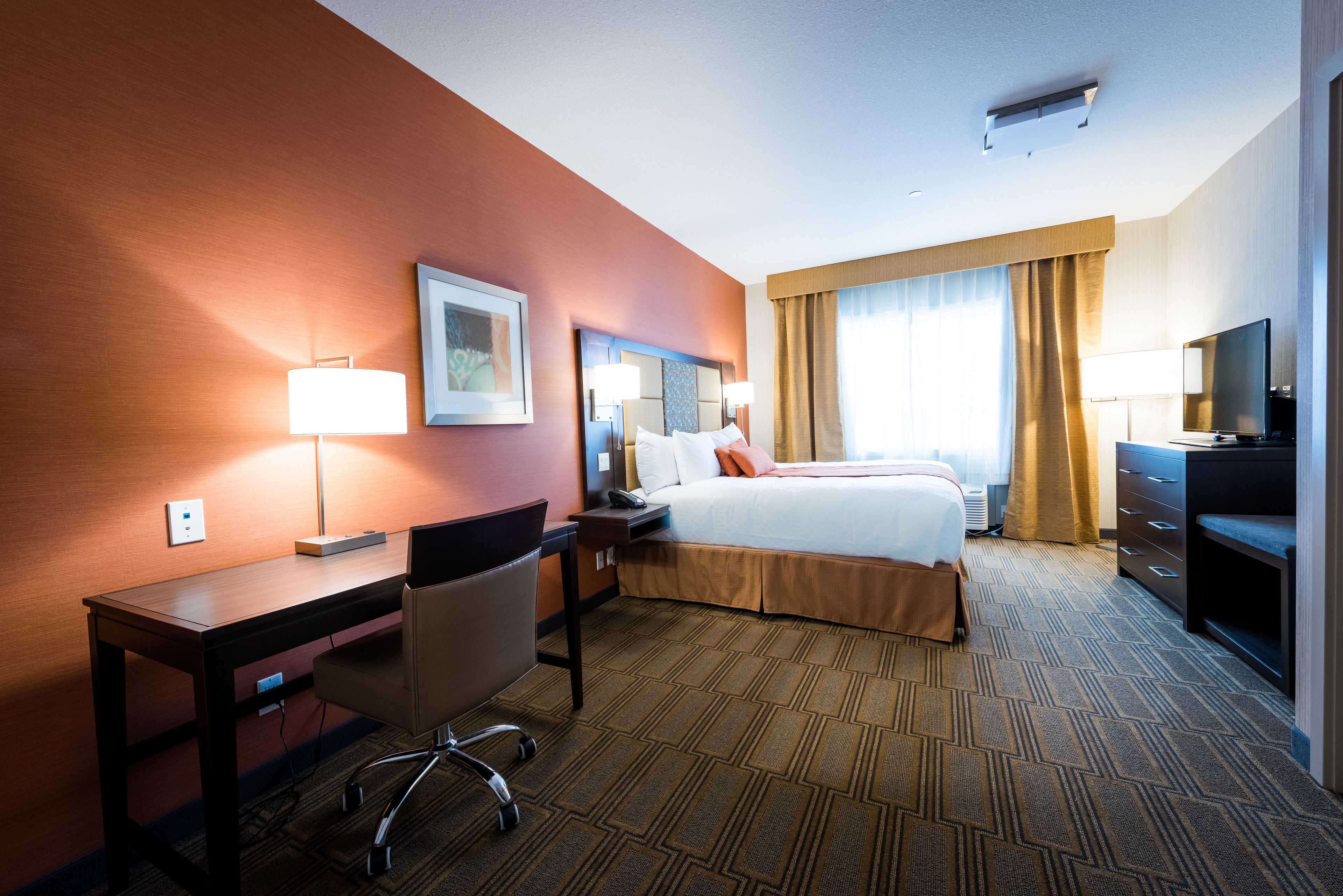 A hotel room with a bed, desk, chair, lamp, and television.