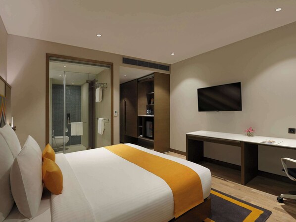 Habitación de hotel con cama, escritorio, televisión y zona de ducha.