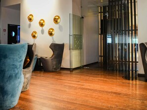 Un vestíbulo moderno con piso de madera, una pared divisoria de vidrio y una zona de estar con dos sillones.