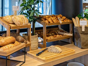 Mostrador de panadería con panes y pasteles varios, tablas de madera para servir y un letrero que indica 100% trigo francés.