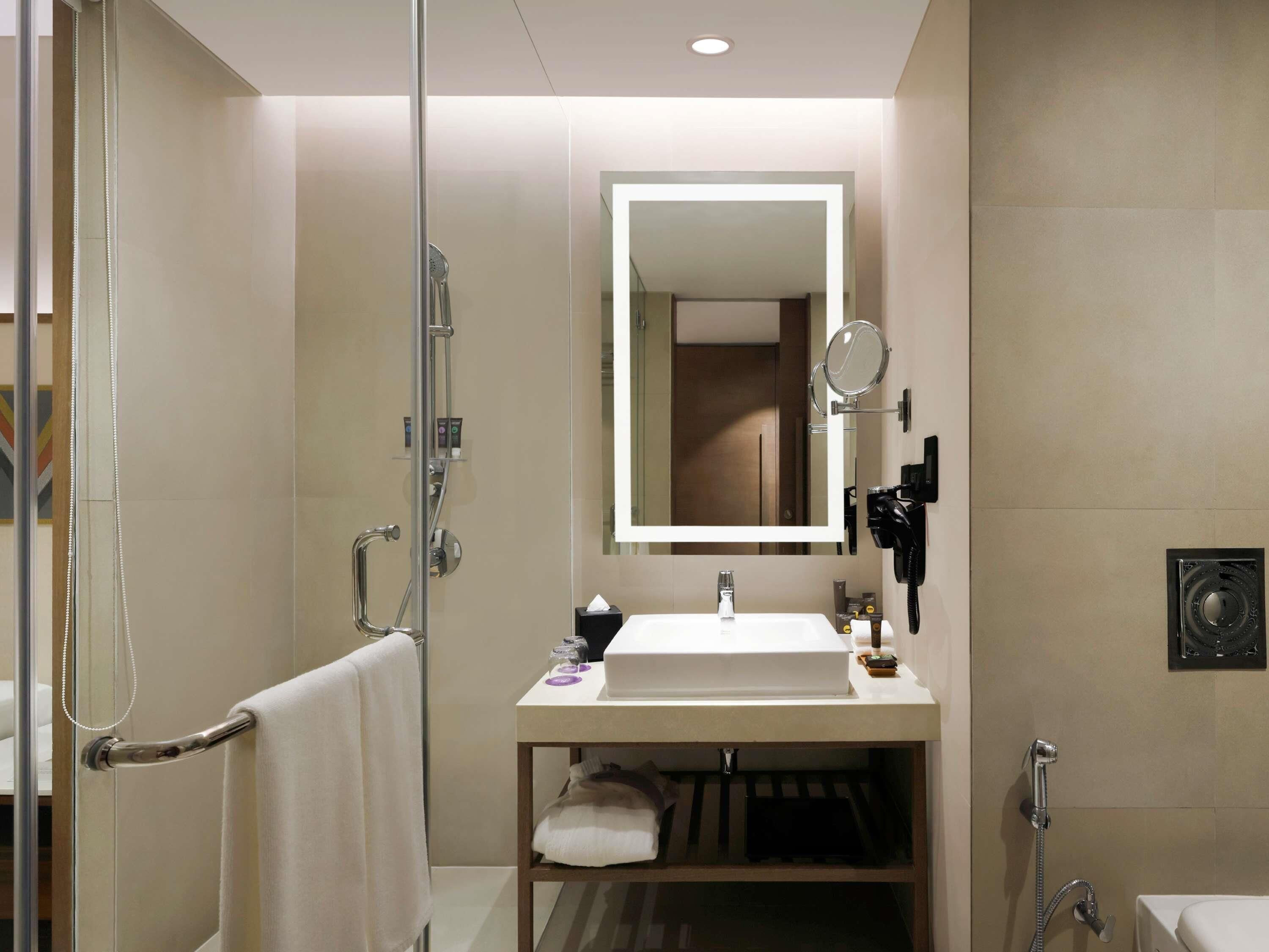 Un baño moderno con cabina de ducha de vidrio, tocador con lavabo y espejo, y un perchero para toallas.