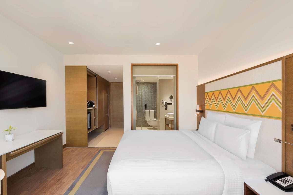 A hotel room with a bed, bedside table, TV, desk, and a bathroom visible through an open door.