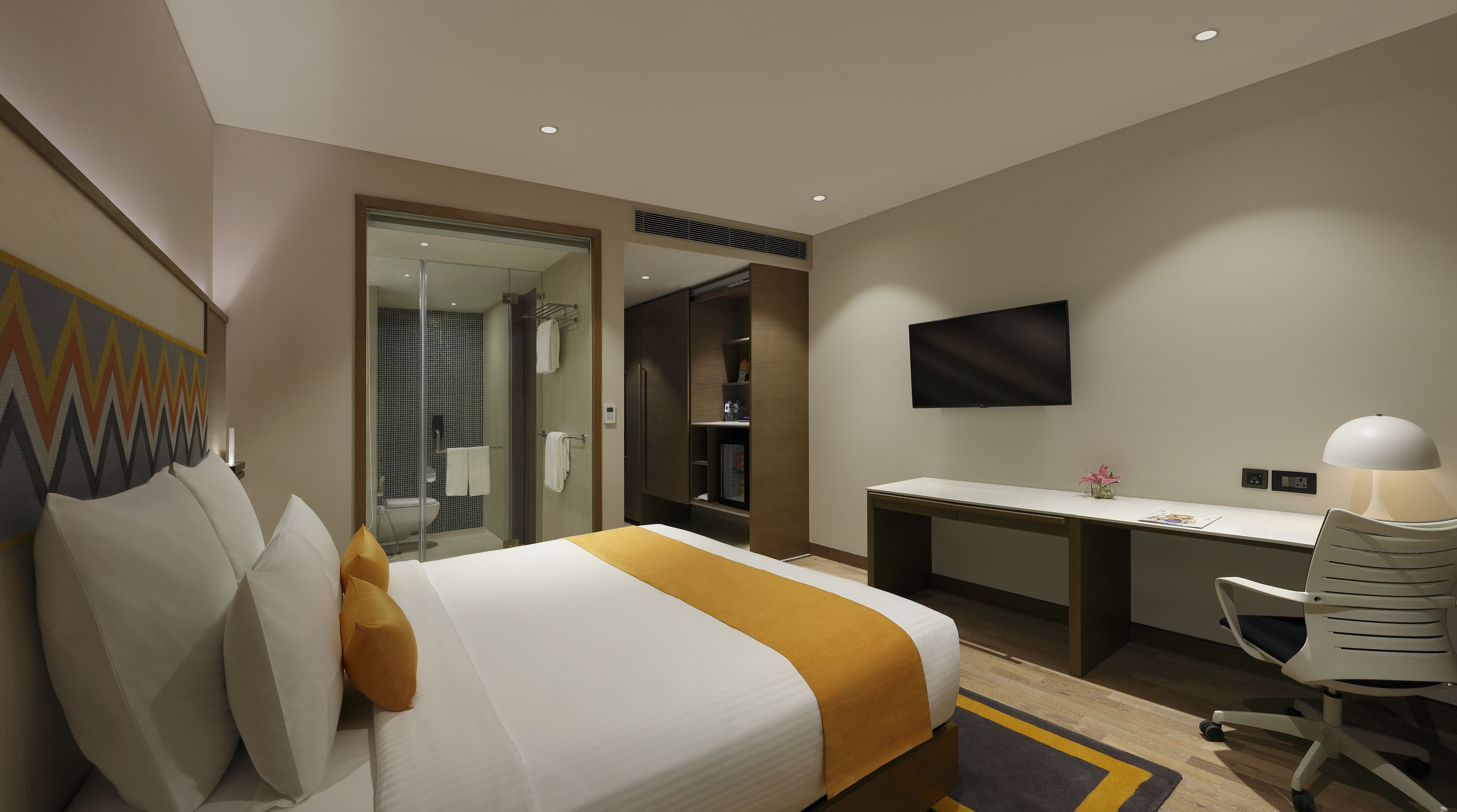 Habitación de hotel con cama, escritorio, silla, televisor y zona de ducha.
