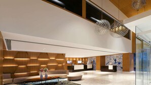 Een moderne hotellobby met een receptiebalie, een zithoek en decoratieve verlichting.