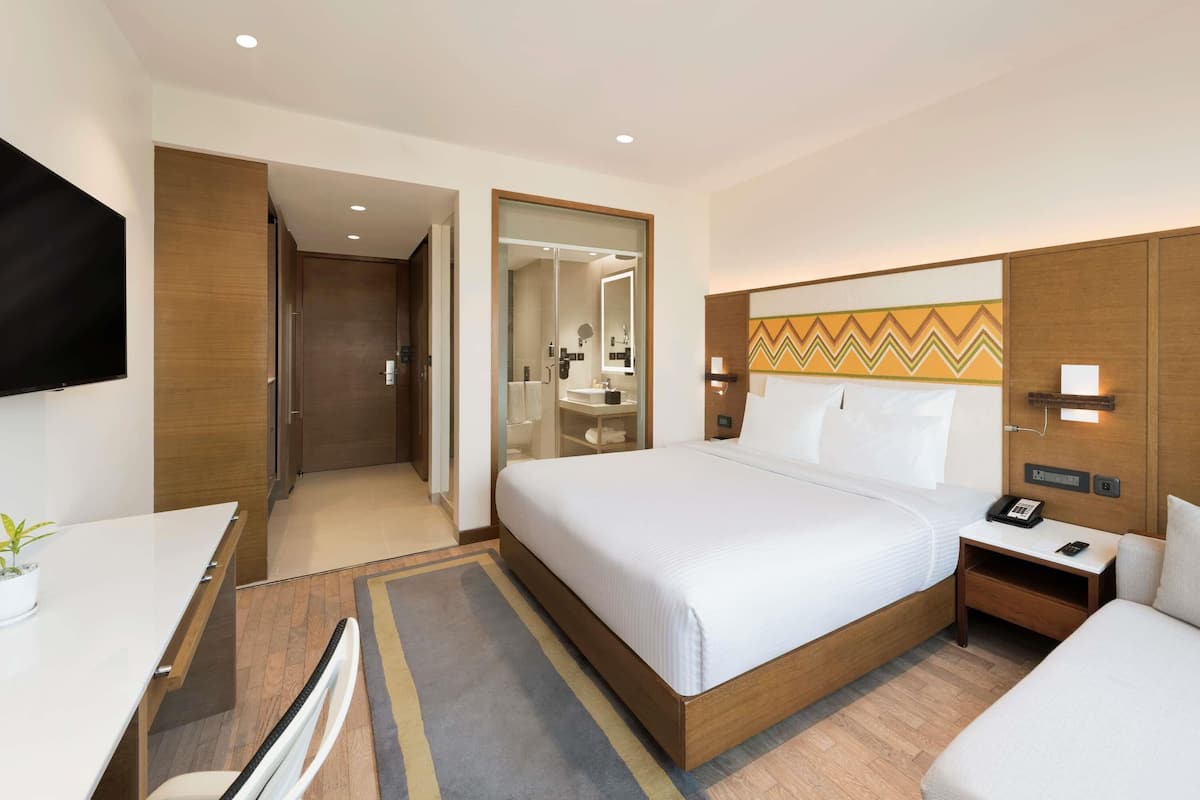 Una habitación de hotel con cama, mesita de noche, televisor y escritorio con silla.