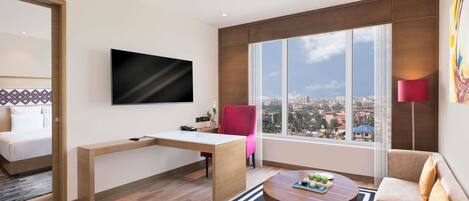 A modern hotel room with a bed, a desk, a TV, a sofa, a coffee table, and a large window with a city view.