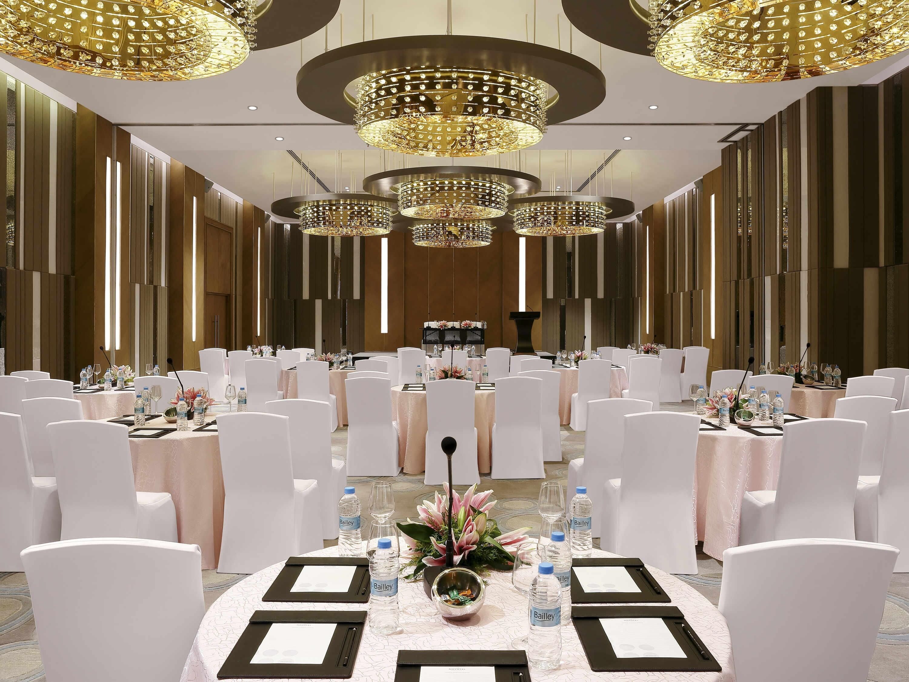 A conference room with round tables, white chairs, water bottles, and a podium.