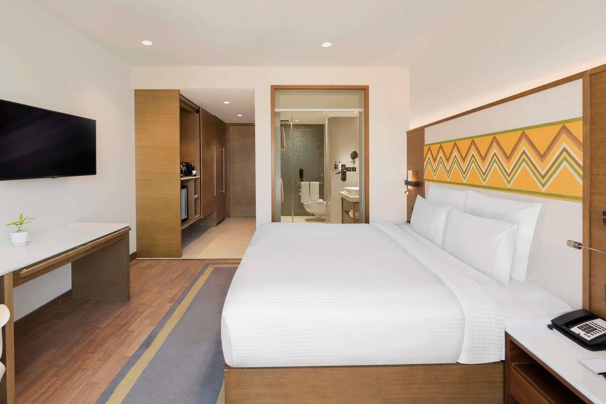 Habitación de hotel con una cama grande, un escritorio, un televisor, un baño y una ducha.