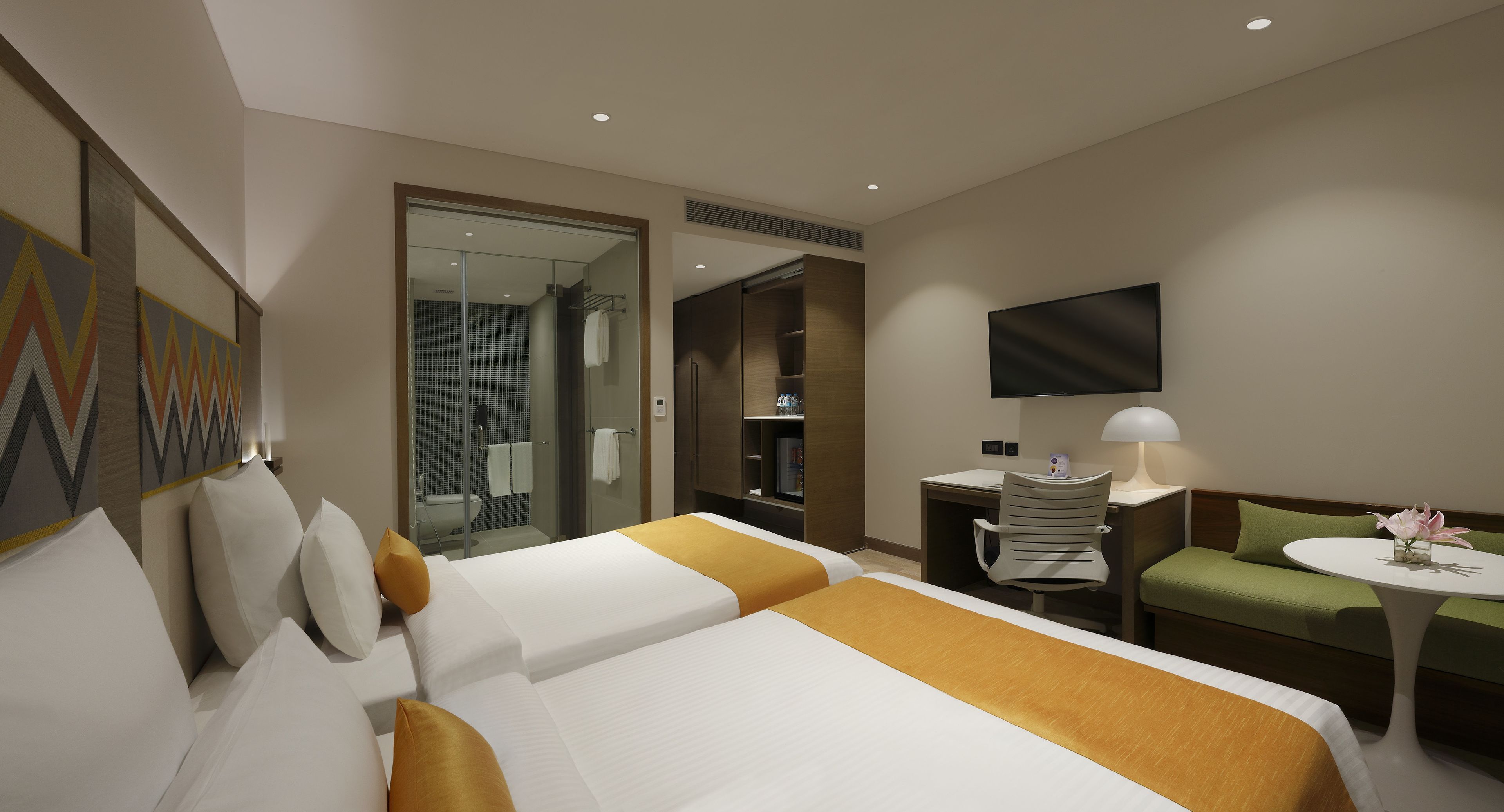 Ein Hotelzimmer mit zwei Betten, einem Schreibtisch, einem Fernseher, einer Sitzecke und einem durchgehenden Tür angedeuteten Badezimmer.