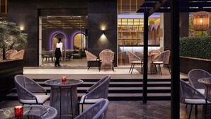 Een zithoek met rieten stoelen en tafels, een receptiebalie en een uitzicht op het restaurant.