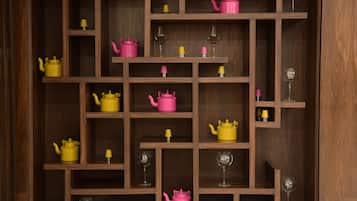 A wooden shelf unit with multiple compartments, each containing a pink teapot, a yellow teapot, and a wine glass.