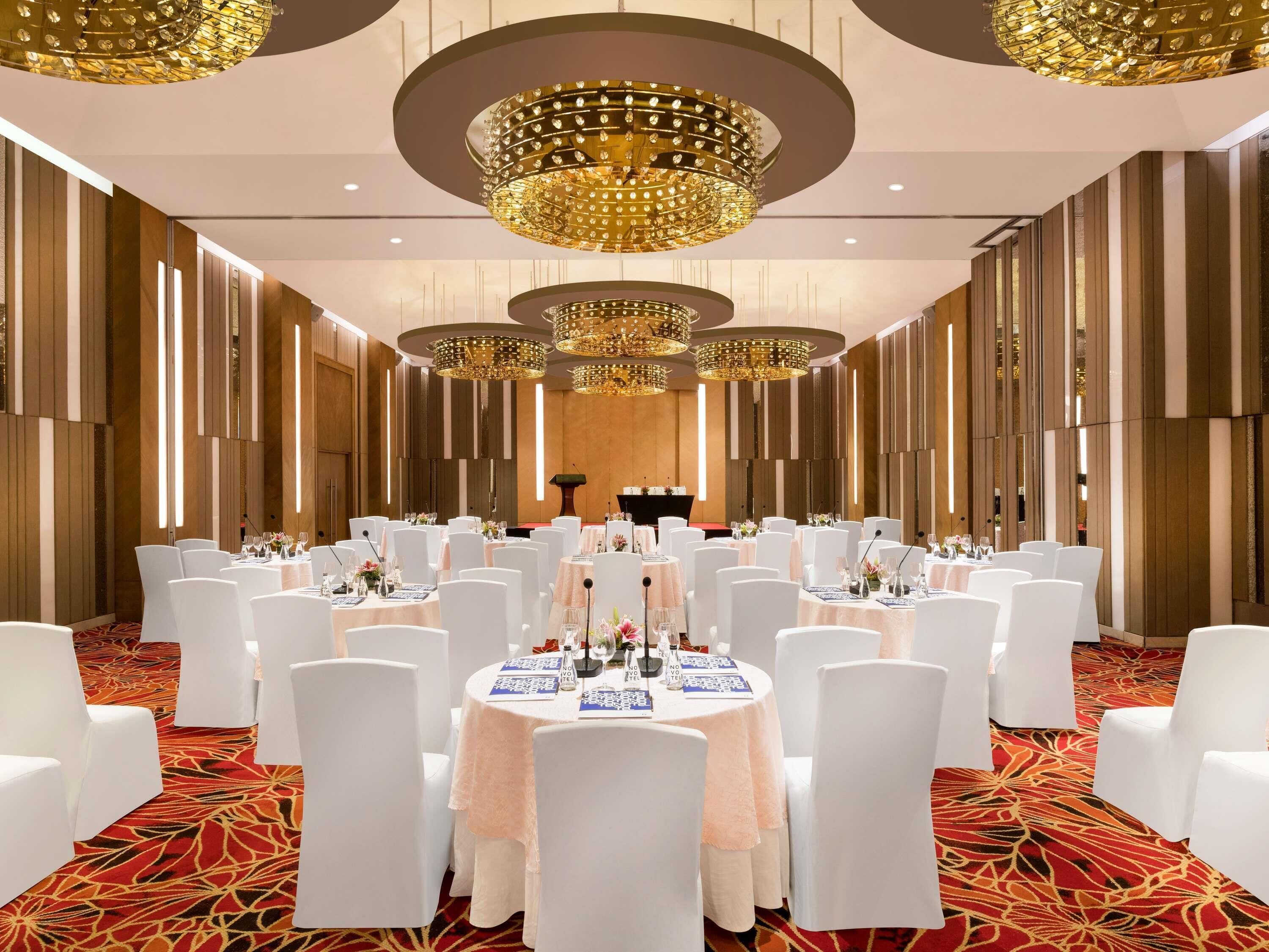 Un salón de banquetes con mesas redondas, sillas blancas y candelabros elaborados.