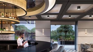 Un área de bar moderna con una lámpara circular, un camarero y vistas a la vegetación a través de amplias ventanas.