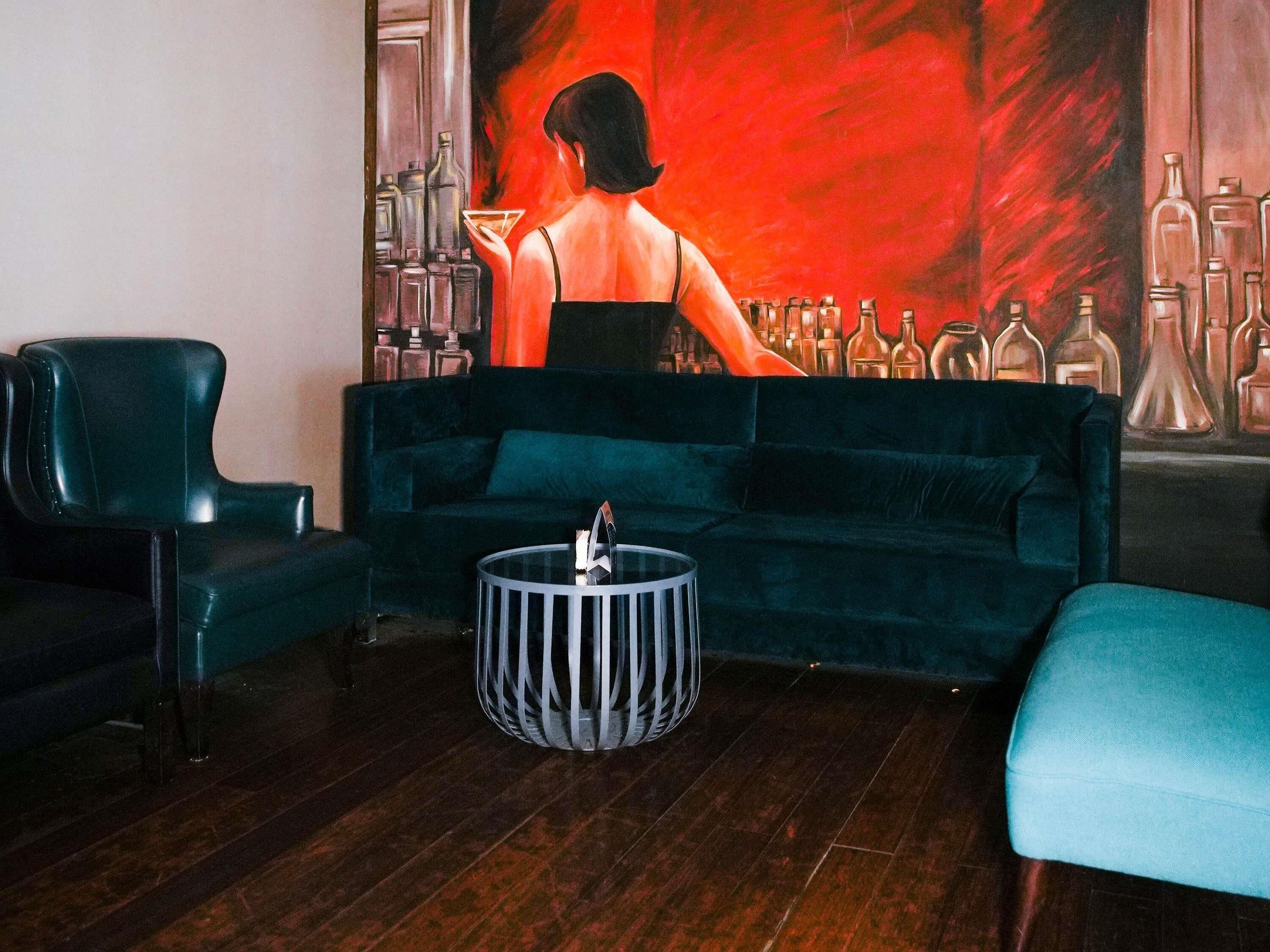 Una habitación con un sofá verde oscuro, una mesita redonda y una zona de bar con botellas.