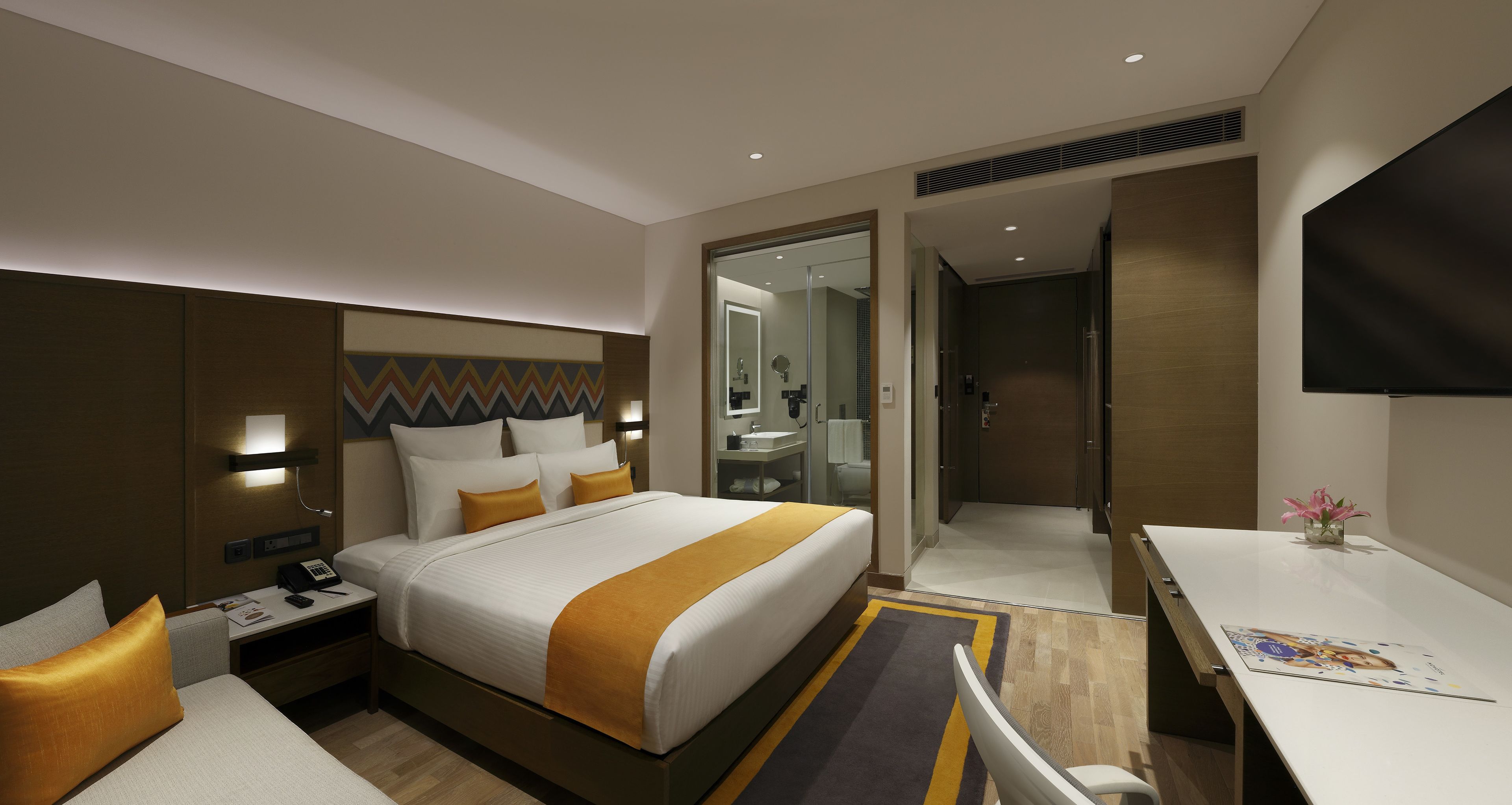Una habitación de hotel moderna con una cama grande, mesitas de noche, un escritorio, un televisor de pantalla plana y un baño visible a través de una puerta abierta.