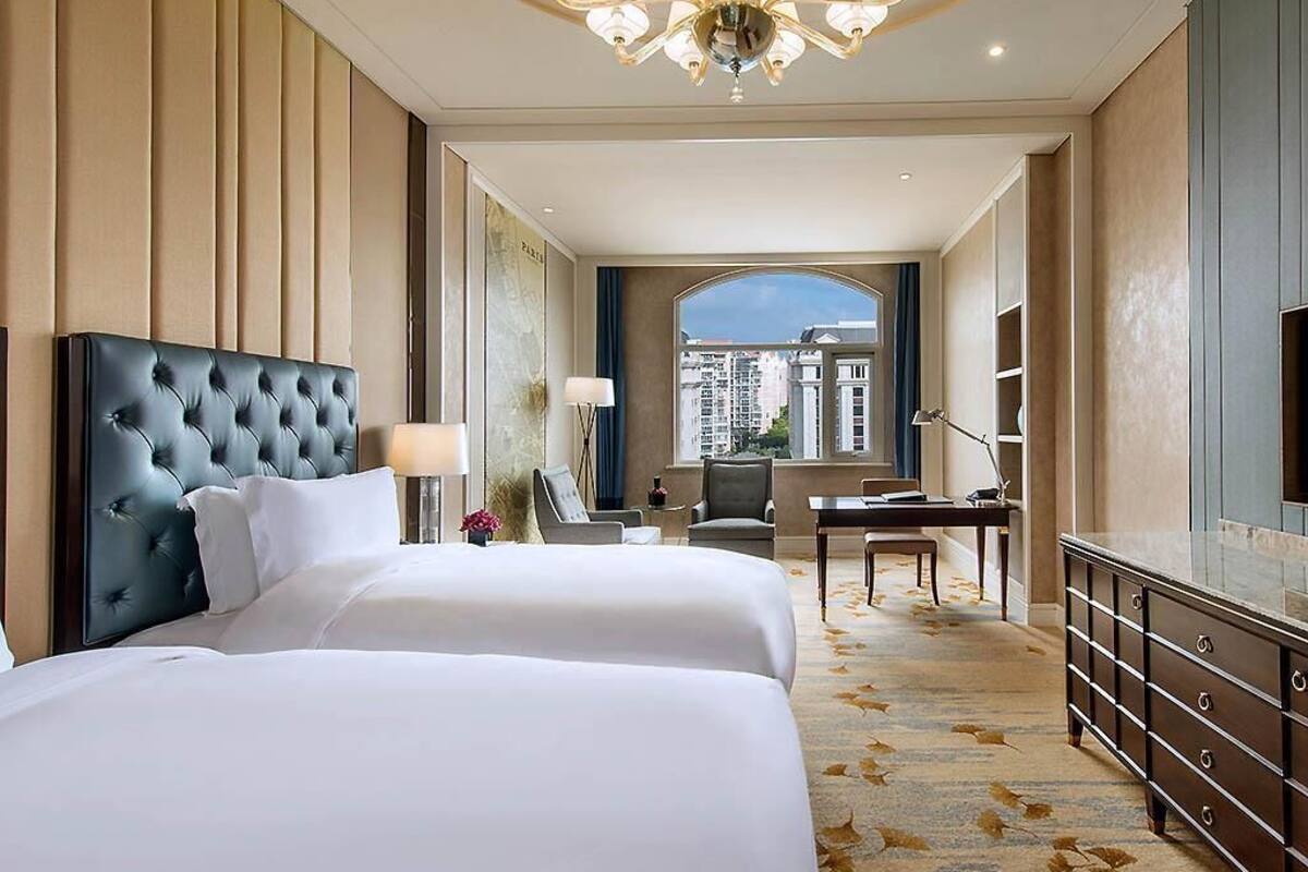 A hotel room with a large bed, a desk, a dresser, and a view of the city.