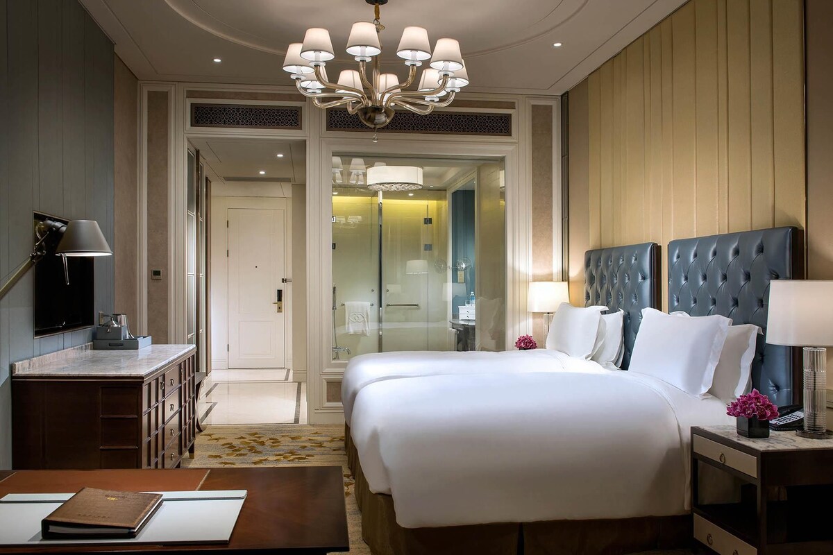 A hotel room with a large bed, a desk, a chair, a television, and a bathroom visible through an open door.