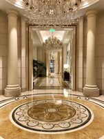 Eine prächtige Eingangshalle mit einem großen, verzierten Chandelier, Marmorsäulen und einem detailreichen, kreisförmigen Bodenmuster.