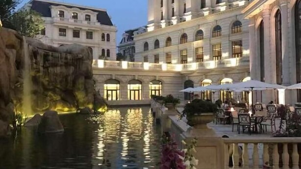 Un grand bâtiment à étages, une cour intérieure agrémentée d’un élément aquatique et des espaces extérieurs aménagés pour s’asseoir.