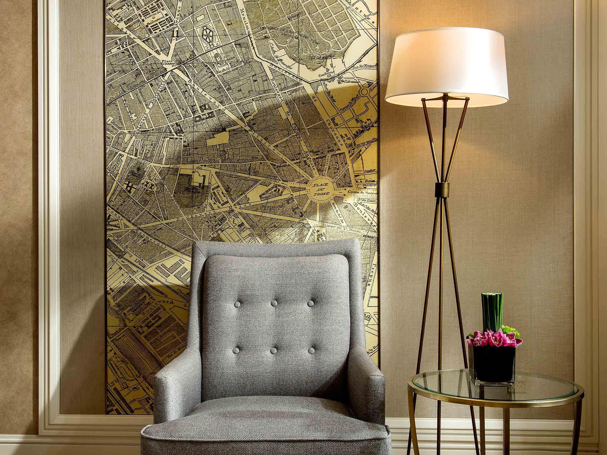 Una habitación con un mural de mapa, un sillón tapizado gris, una lámpara de pie y una pequeña mesa redonda con un florero.