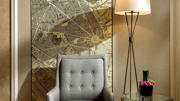 Una habitación con un mural de mapa, un sillón tapizado gris, una lámpara de pie y una pequeña mesa redonda con un florero.