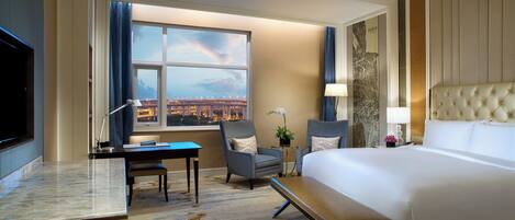 Ein Hotelzimmer mit einem großen Bett, einem Schreibtisch, einem Stuhl, einer Bank, einem Fernseher und einem Fenster mit Blick auf die Stadt.
