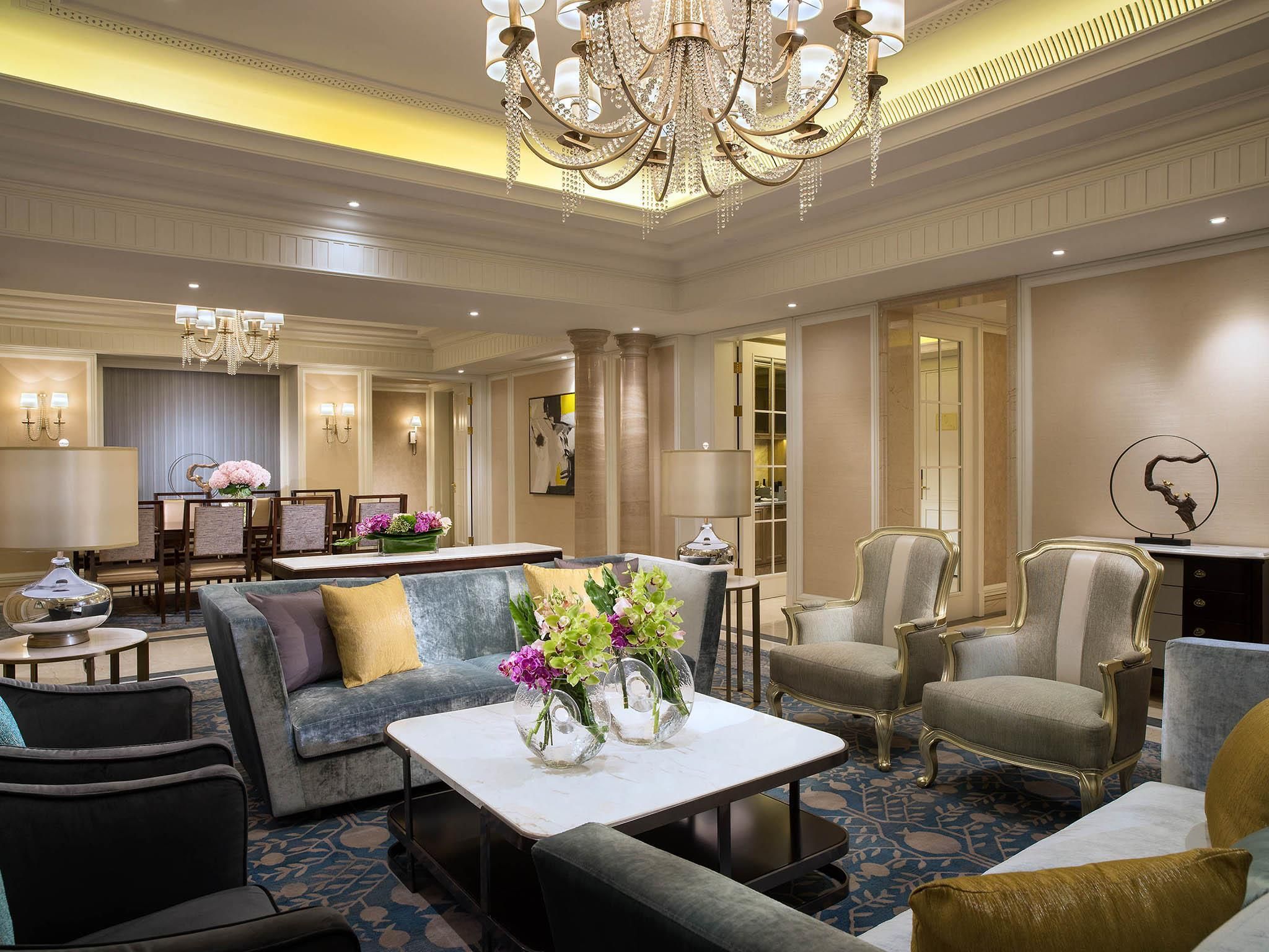 A spacious hotel lobby with a chandelier, seating arrangements, and a reception desk.