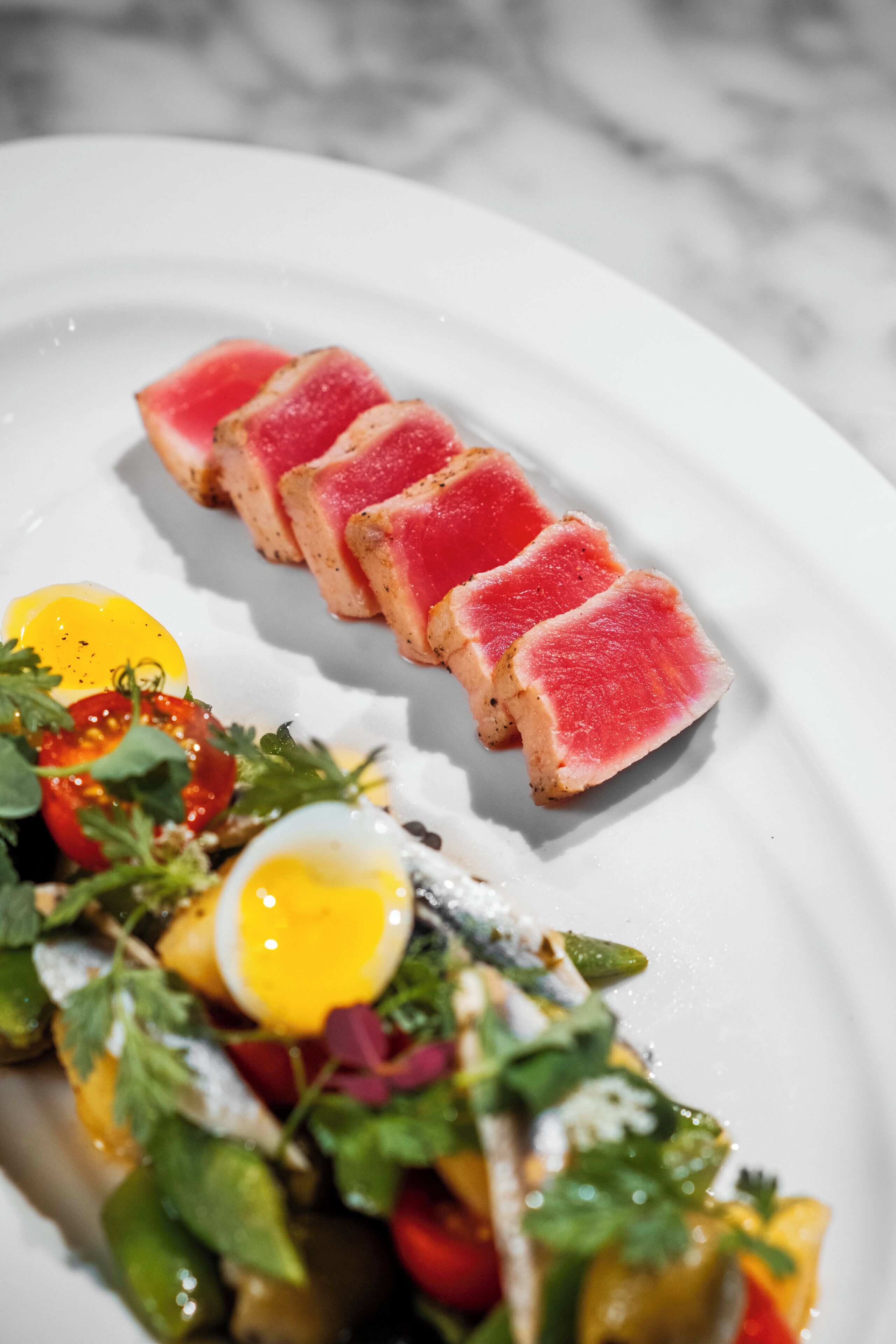 Een bord met eten, inclusief plakjes roze vlees, een gekookt ei en een salade met sla en tomaten.