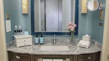 Une salle de bain avec un lavabo en marbre, un miroir, un vase de fleurs et des articles de toilette posés sur le comptoir.