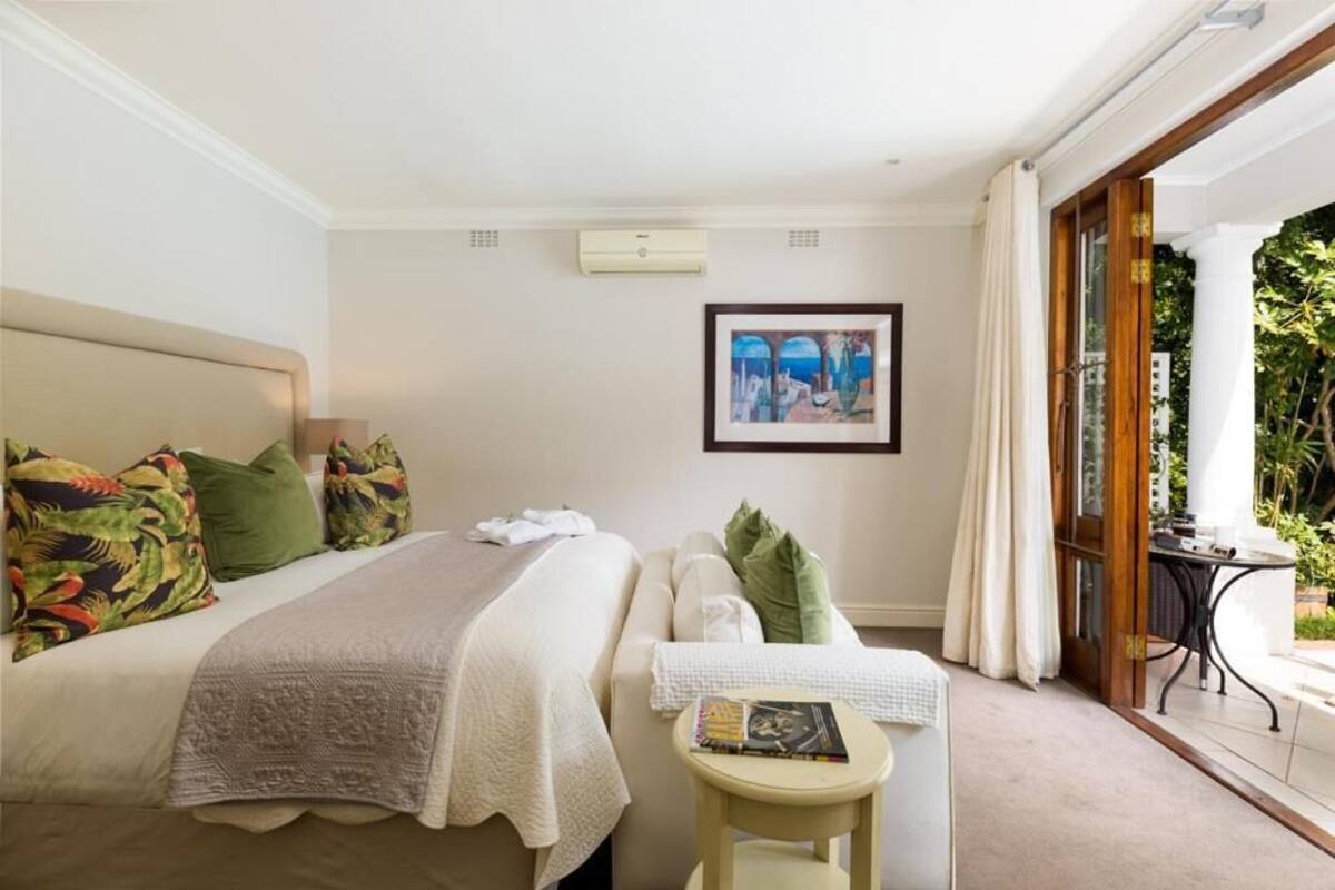 Ein Hotelzimmer mit Bett, kleinem Tisch, einem gerahmten Bild an der Wand und Blick auf Grünfläche.
