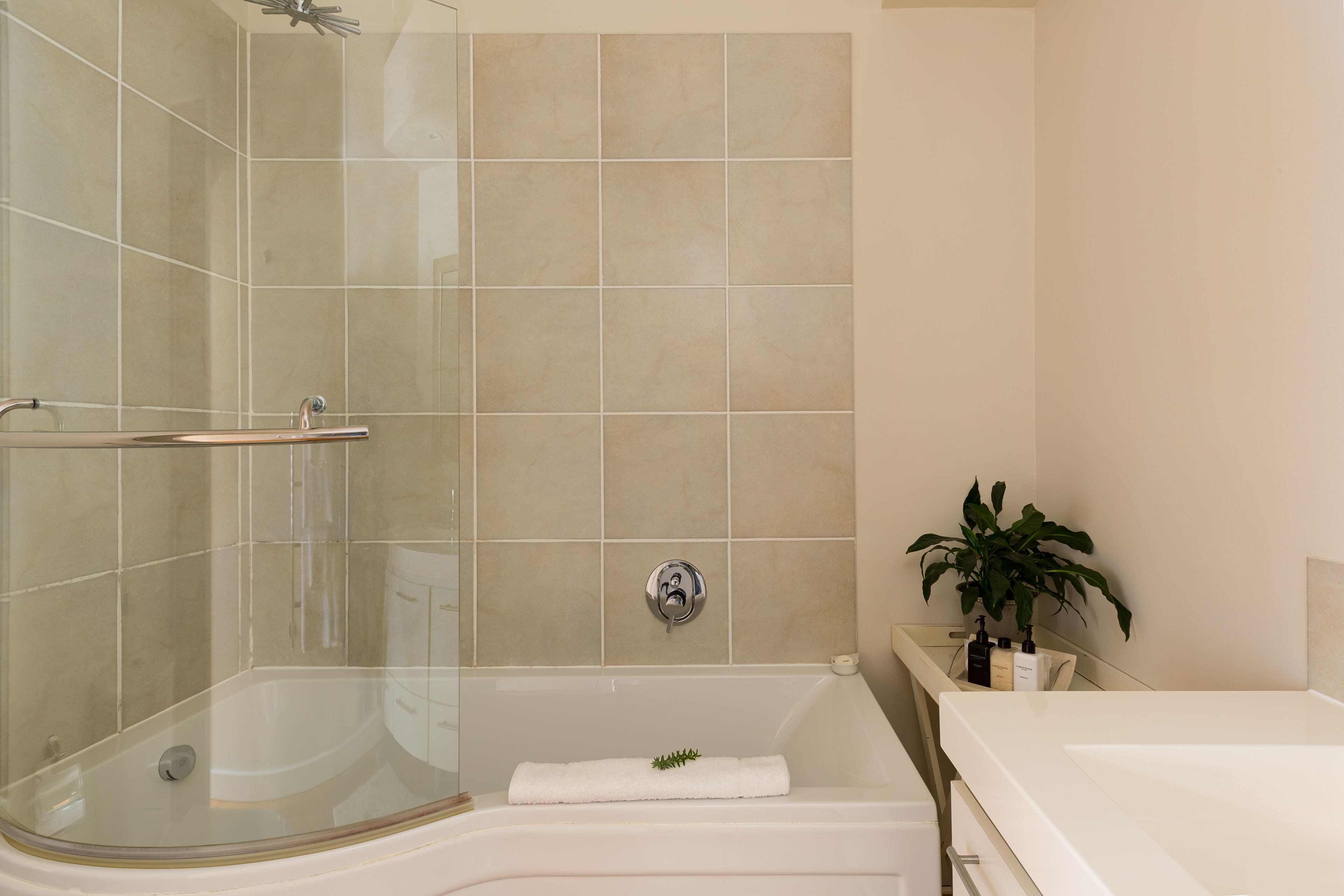 A bathroom with a glass-enclosed shower, a bathtub, and a sink with toiletries.