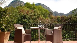 Een terras met rieten stoelen en een tafel, met uitzicht op een bergachtig landschap.