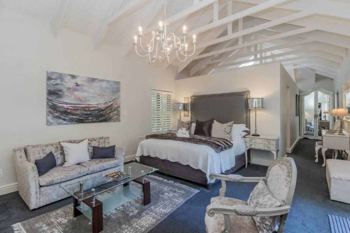 Ein geräumiges Schlafzimmer mit einem großen Bett, einer Sitzecke mit Sofa und Sessel, einem Glastisch und einer Kronleuchter.