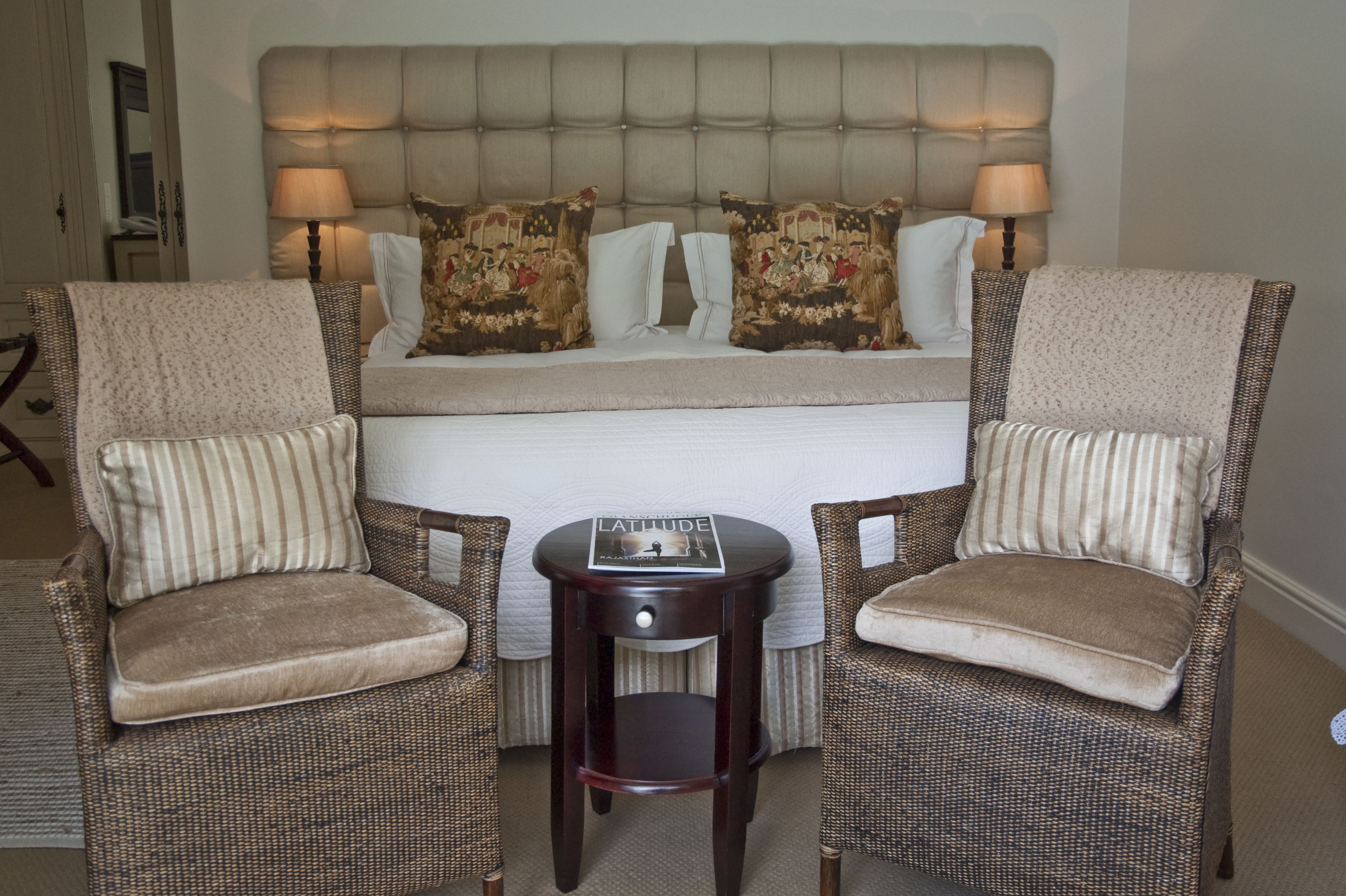 A bedroom with a large bed, two upholstered chairs, a small side table, and two bedside lamps.
