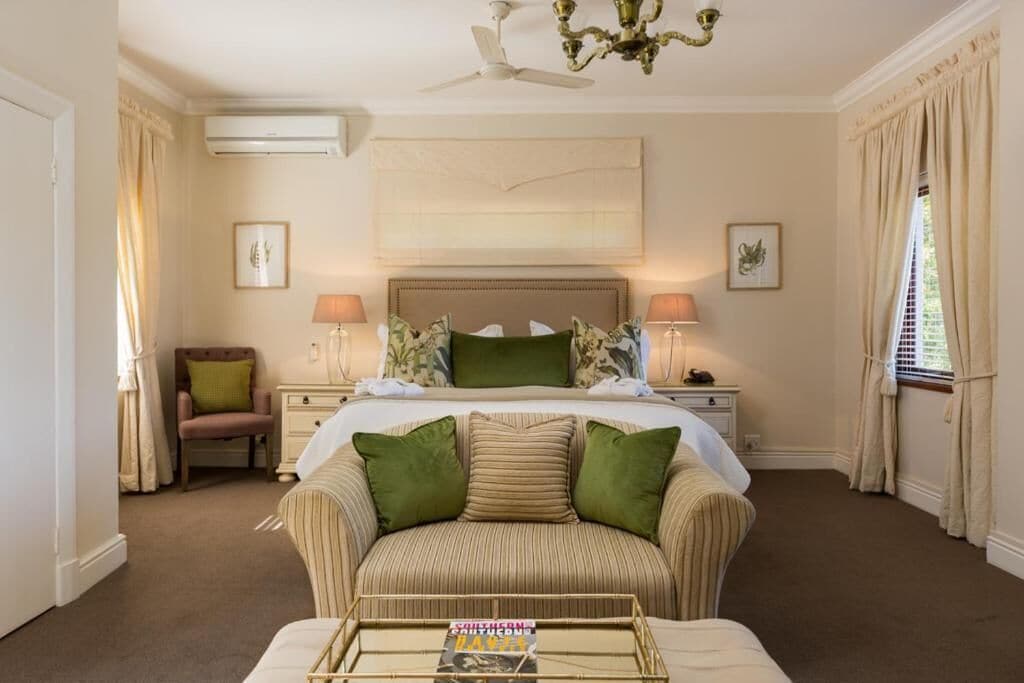 Een hotelkamer met een groot bed, twee nachtkastjes met lampen, een groene bank en een plafondventilator.