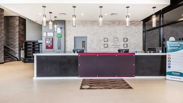 Un espace d’accueil moderne avec un comptoir de réception en marbre, des luminaires suspendus et un paillasson d’entrée.
