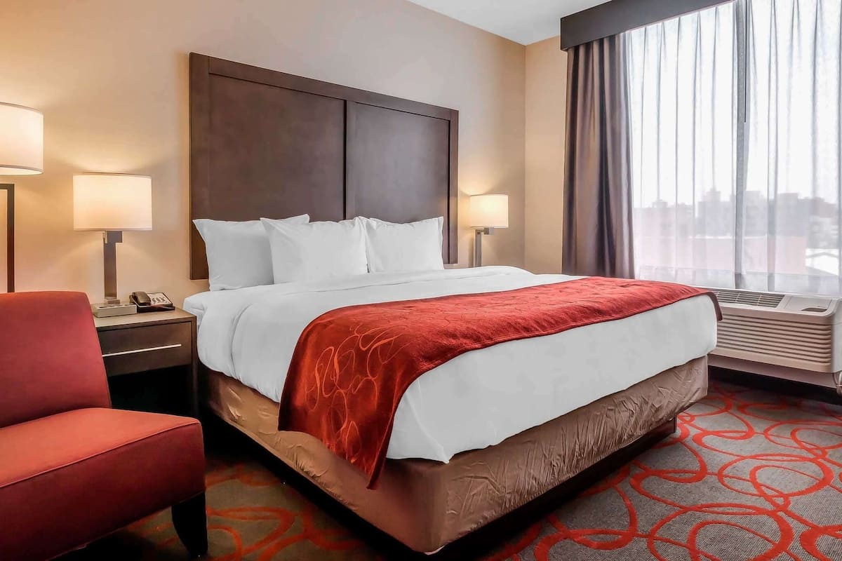 Una habitación de hotel con una cama grande, dos lámparas de noche, una silla roja y una ventana con cortinas.