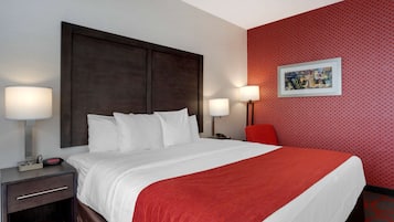A hotel room with a large bed, two bedside tables, a red wall, and a framed picture on the wall.
