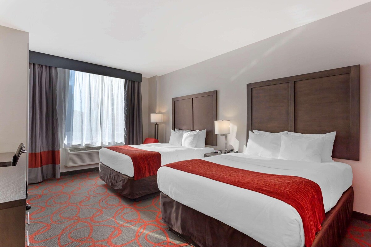 A hotel room with two beds, a desk, and a window with curtains.