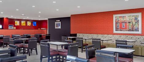 Un restaurante con varias mesas y cabinas, una pared de acento roja y un cuadro en la pared.